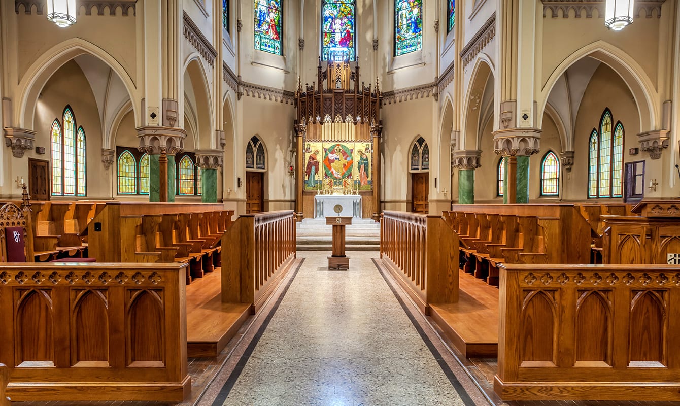 The inside of a church with wooden pews and stained-glass windows.