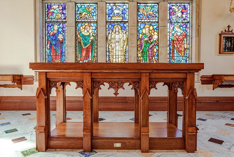 A wooden altar from St. Mark's Episcopal Church with stained glass windows behind it.
