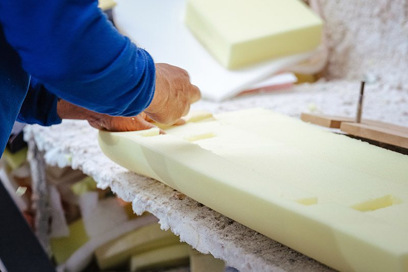 A worker carefully carves a pew back out of foam.